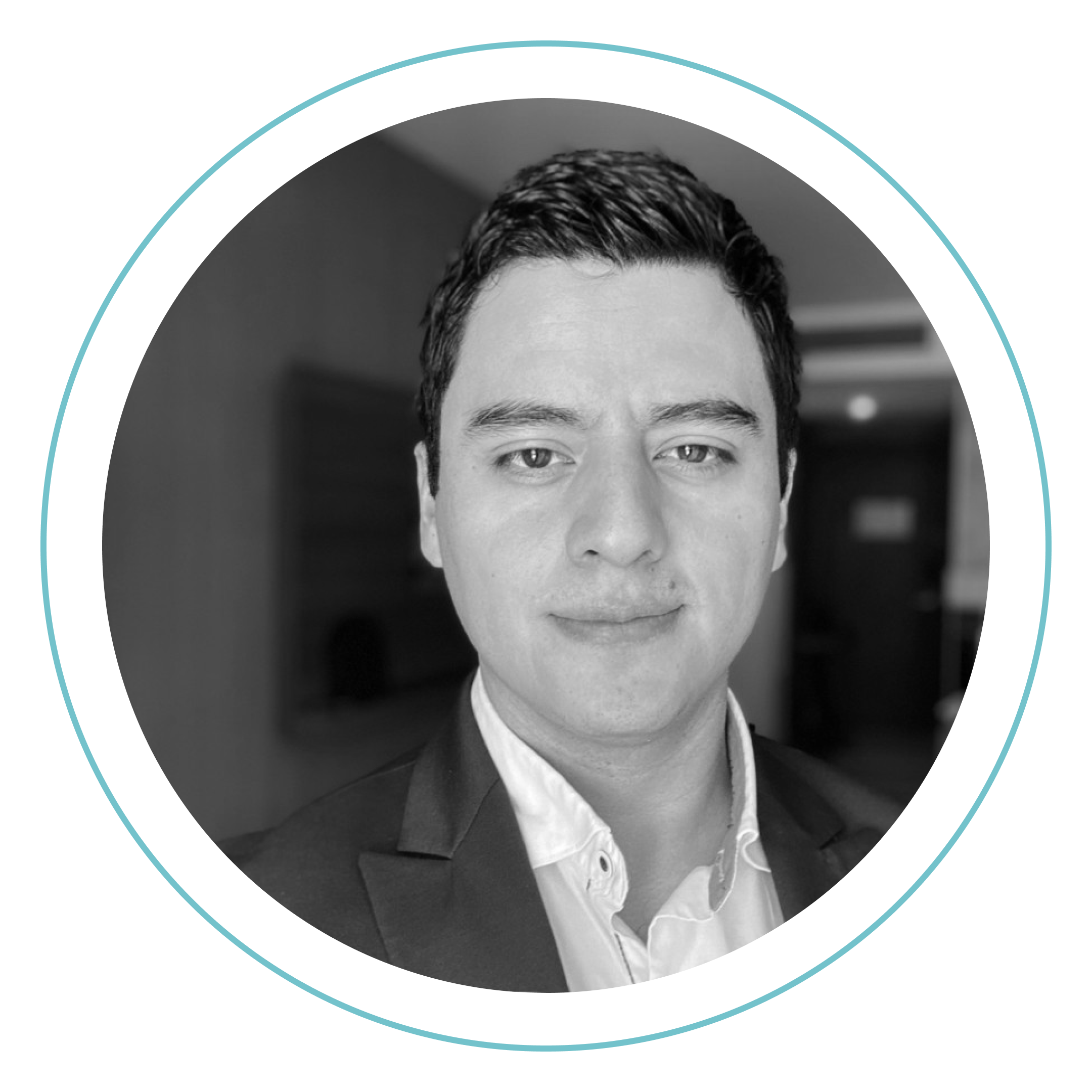 Fotografía en blanco y negro de un hombre con el pelo corto y oscuro, vestido con traje de chaqueta y camisa blanca, sonriendo ligeramente. El fondo está difuminado y la foto está enmarcada por un contorno circular azul.
