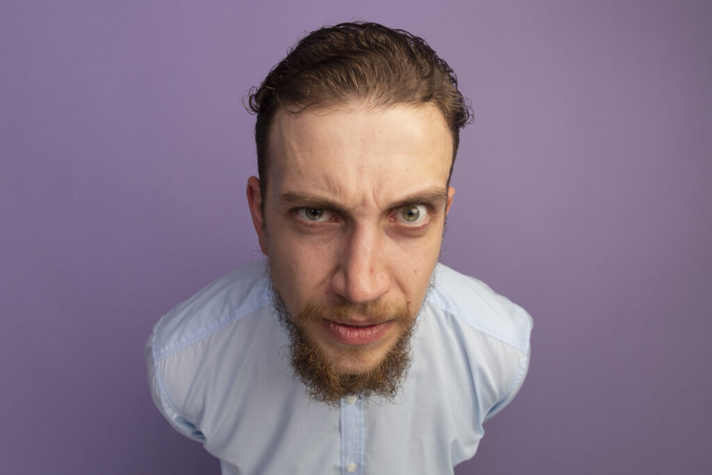 Un hombre con barba y bigote, que representa al nuevo consumidor energético, viste una camisa azul claro y, de pie sobre un fondo morado, mira directamente a la cámara con una ceja levantada y expresión inquisitiva.