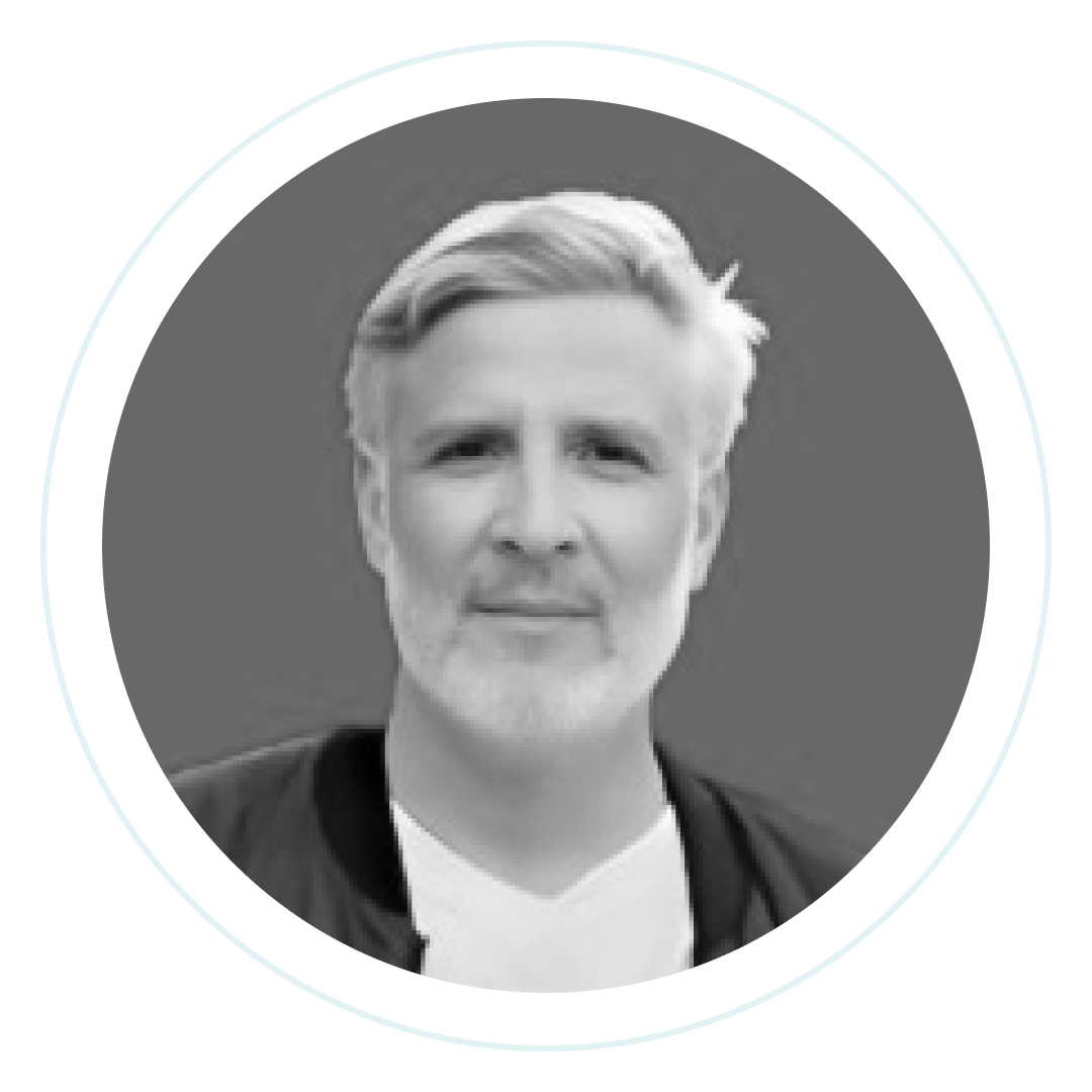 Retrato en blanco y negro de un hombre de mediana edad con pelo claro y barba, vestido con camisa blanca y chaqueta oscura, que mira a la cámara con expresión neutra. La imagen está en un marco circular.