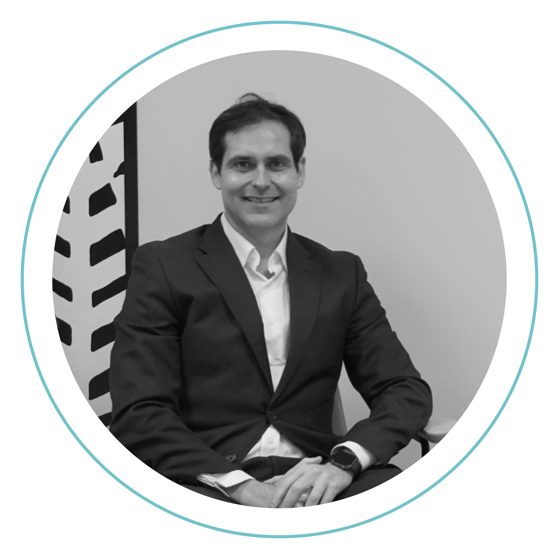 Fotografía en blanco y negro de un hombre trajeado sentado y sonriendo a la cámara, con un fondo de motivos geométricos y un borde circular que enmarca la imagen.