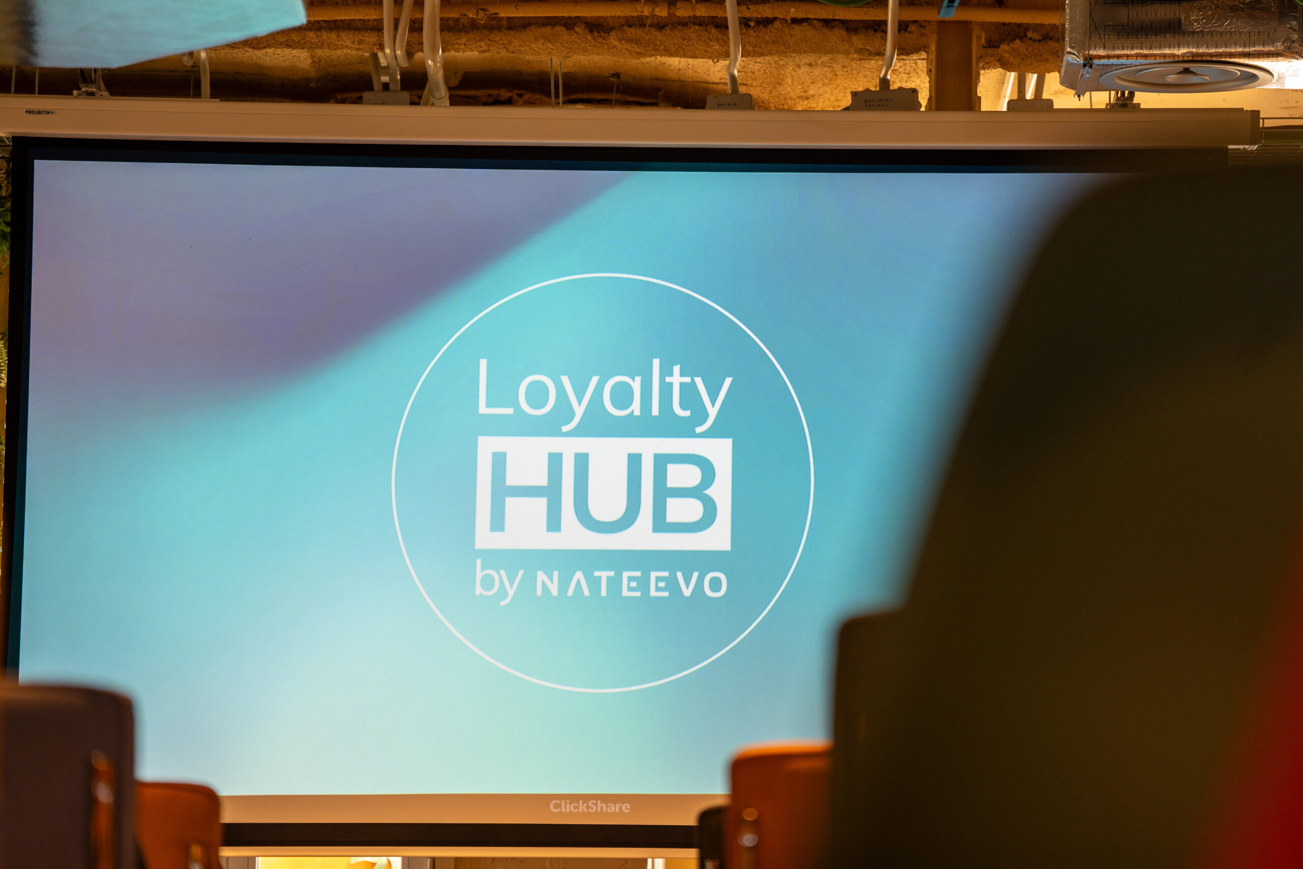 Una pantalla de presentación muestra el texto Loyalty HUB by NATEEVO en letras blancas sobre fondo azul, destacando el concepto 