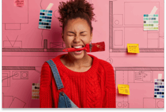 Una mujer con jersey rojo y mono vaquero sostiene un pincel en la boca, los ojos cerrados juguetonamente, de pie ante una pared rosa cubierta de bocetos, muestras de pintura y notas adhesivas sobre novedades de Salesforce en Dreamforce 2025.