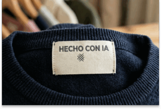 Primer plano de una etiqueta de ropa cosida en una prenda de punto azul oscuro, que muestra el texto HECHO CON IA sobre un pequeño símbolo decorativo, destacando la creatividad digital inspirada en la próxima Ley de IA.