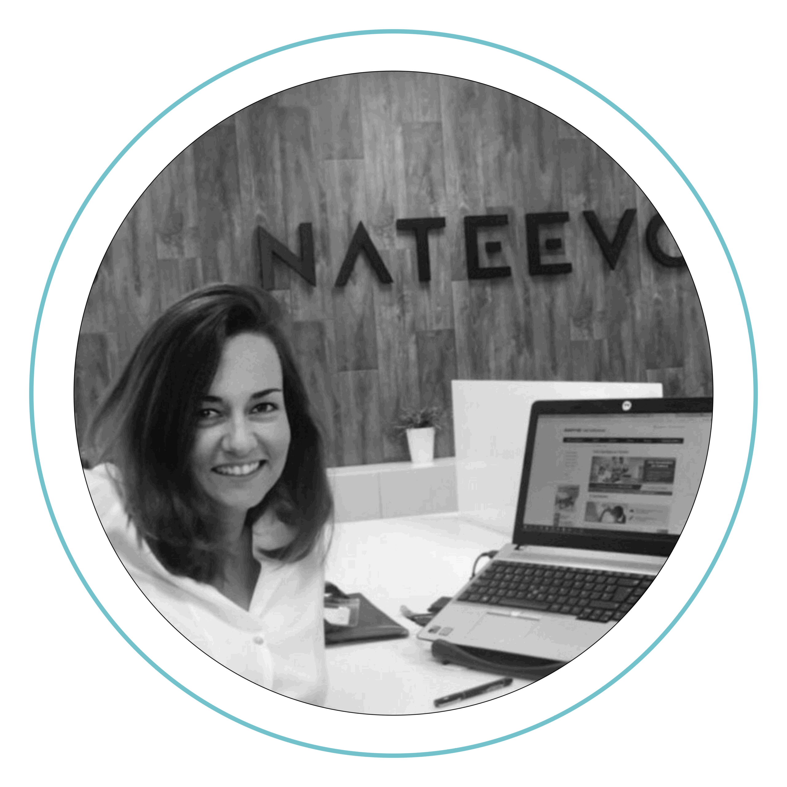 Una mujer que sonríe sentada en su escritorio, junto a un ordenador portátil, un bloc de notas y un bolígrafo. Detrás de ella hay una pared de madera con las letras «NATEEVO» escritas en grande. La imagen es en blanco y negro y tiene un borde circular.